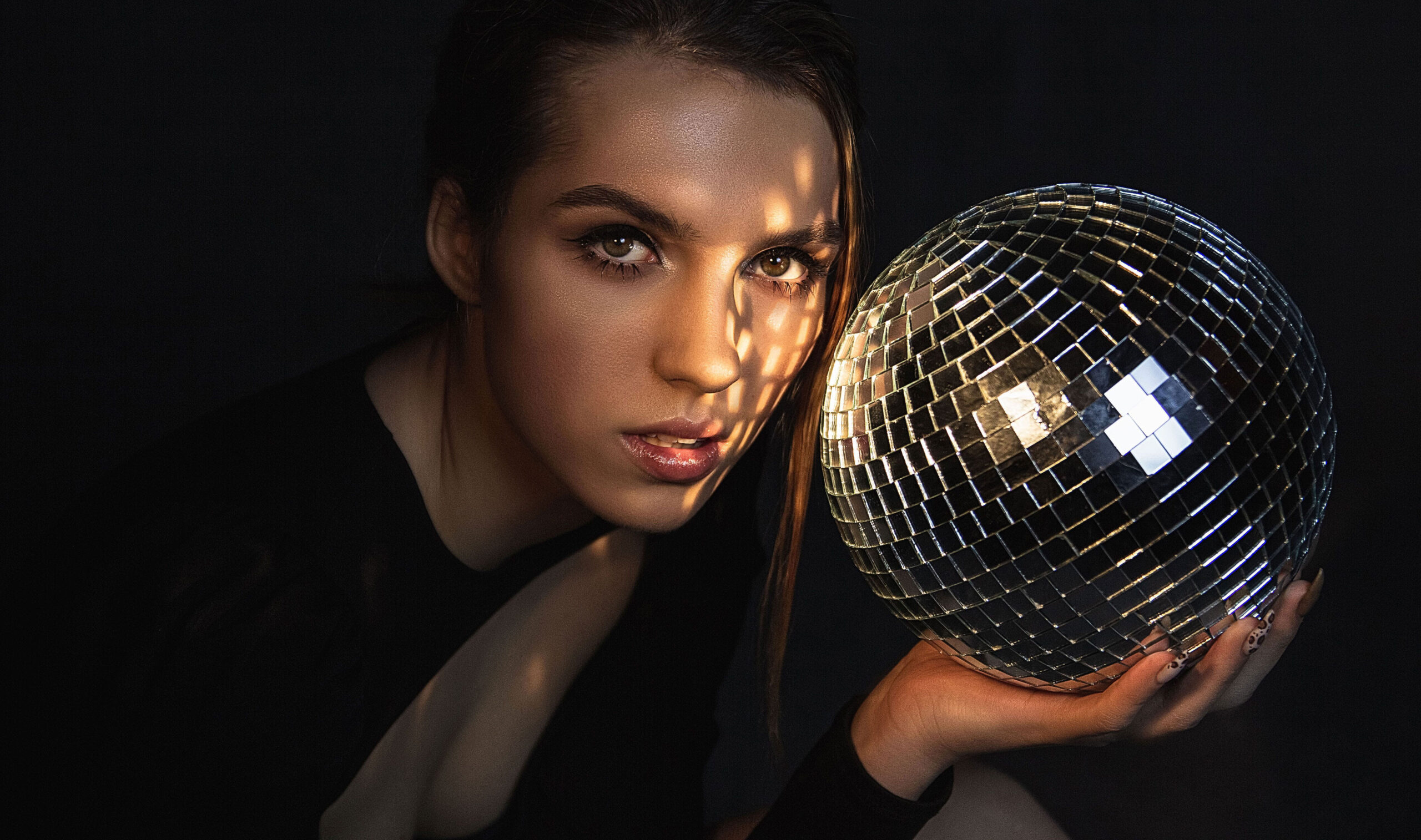A woman playfully holds a disco ball in front of her face, creating a whimsical and reflective moment.